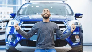 Happy man in front of a car to augment the article about getting a cheap rent to buy cars.